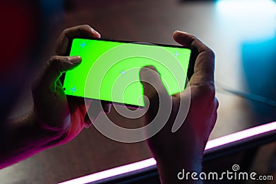 Shoulder shot first person view of gamer playing video game on green screen mobile phone while talking on headphones at esports Stock Photo