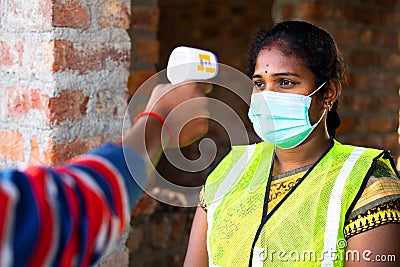 shoulder shot of man checking body tempreture of woman worker with medical face mask at workplace - concept of covid19 Stock Photo