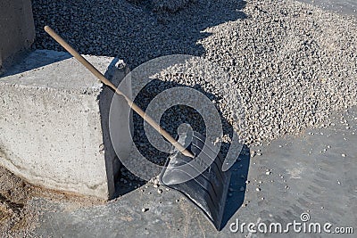 Shovel, leaning against concrete block next to pile of gray gravel, and tracks of truck tires are visible on cement floor screed. Stock Photo