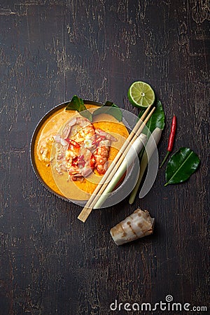 Shrimps Tom Yam Kung in grey bowl with thai spices on autentic tray top view, wooden background Stock Photo