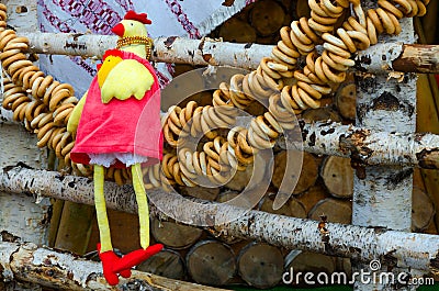 Shrovetide festivities. Decor of trade places. Toy-rooster and bundle of bagels, hanging on birch fence Editorial Stock Photo