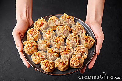 Shumai or Kanom Jeeb or Steamed Pork and Shrimp Dumplings on a black plate in female hands on dark backdrop. Chinese food. Asian Stock Photo