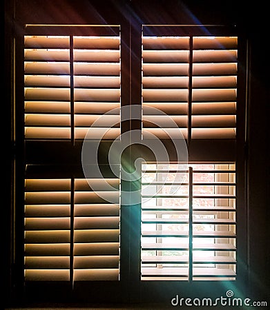 Shuttered window with one pane open letting through rays of light and a faint image of autumn leaves outside Stock Photo