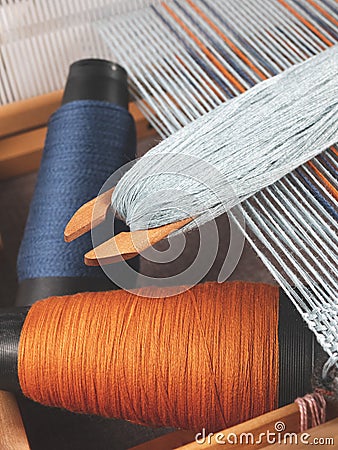 Shuttle with blue thread and two bobbins with indigo and orange yarns for weaving striped textile Stock Photo