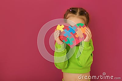 A shy lady holds heart with puzzle pieces covering her face from embarrassment Stock Photo