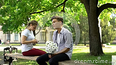 Shy teen with flowers sitting next to lady, surfing net on phone, hesitation Stock Photo