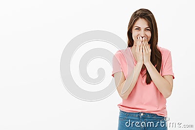 Shy and timid cute european female in pink t-shirt and jeans, chuckling and covering mouth with palm, laughing quietly Stock Photo