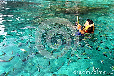 Sian man in orange life jacket with diving mask snorkeling among many Indo-Pacific sergeant fish on Andaman Sea Editorial Stock Photo