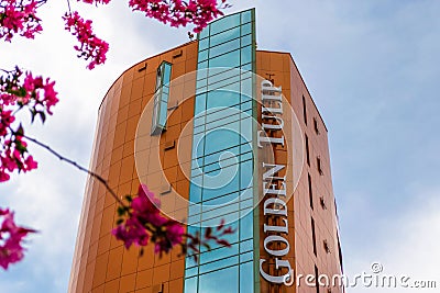 Golden Tulip Ana Tower hotel with its panoramic elevator, as seen from the street, framed by pink flowers Editorial Stock Photo