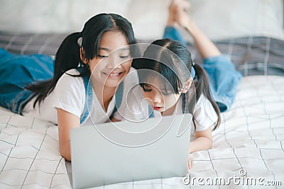 Sibling Asian girl child on the bed and learning online on a laptop Internet. Virtual class lesson on video during self isolation Stock Photo