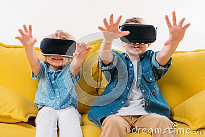 siblings gesturing and using virtual reality headset while sitting Stock Photo