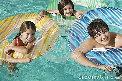 Siblings With Inflatable Rafts Enjoying Together In Swimming Pool Stock Photo
