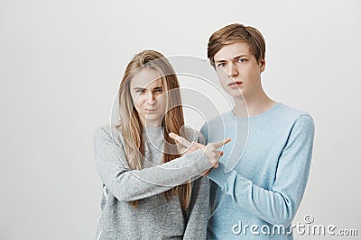 Siblings trying to accuse each other in front of angry mom. Serious unhappy couple with fair hair, frowning and pointing Stock Photo