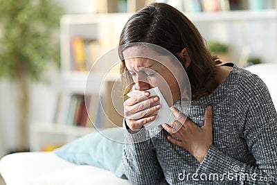 Sick adult woman coughing covering mouth with tissue at home Stock Photo