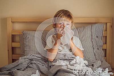 Sick boy coughs and wipes his nose with wipes. Sick child with fever and illness in bed Stock Photo