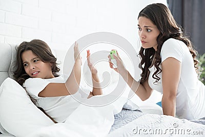 Sick cute teen girl lying in bed refusing her mother to take medicine Stock Photo