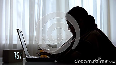 Sick female freelancer working on laptop early in morning and drinking tea Stock Photo