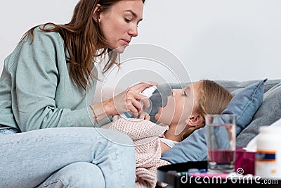 Sick girl lies on the couch and her mother sprays medicine into her mouth Stock Photo