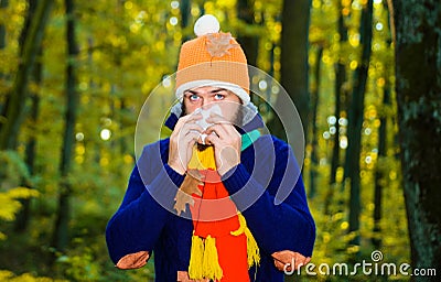 Sick man in autumn park sneezing in napkin. Guy coughing. Influenza, illness, sick, cold. Coronavirus epidemic. Male Stock Photo