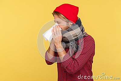 Sick man in hat and warm scarf coughing sneezing tissue, feeling unwell with runny nose, sore throat, suffering allergy Stock Photo