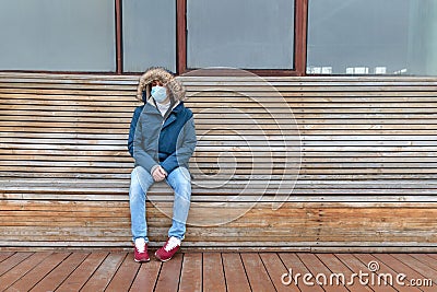Sick man with hood sitting alone on bench, wearing facial mask. Life in isolation, quarantine, coronavirus pandemic Stock Photo