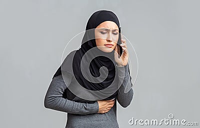 Sick muslim woman suffering from stomach pain, calling doctor for help Stock Photo