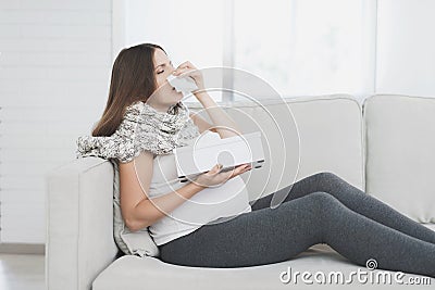 Sick pregnant woman sitting at home on the couch. She flies herself into a paper napkin. Stock Photo