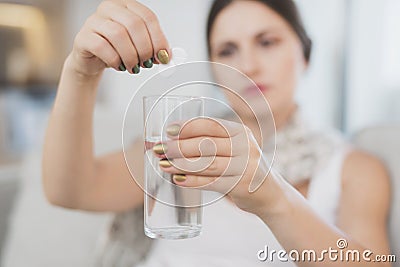 Sick pregnant woman sitting at home on the couch. She throws two tablets into a glass of water Stock Photo