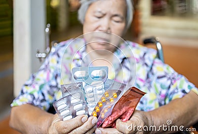 Sick senior woman holding medicine pills in wheelchair,sad female elderly showing a lot of drugs,medication to treatment her Stock Photo