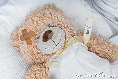 Sick Teddy bear with plaster and thermometer is lying in bed Stock Photo