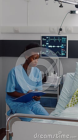 Sick woman resting in bed while afro-american nurse monitoring disease Stock Photo