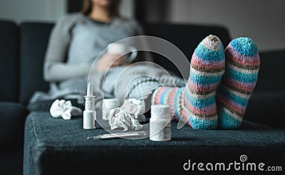 Sick woman resting on couch holding hot cup of tea. Ill person with flu, cold, fever or virus sitting on sofa at home in winter. Stock Photo