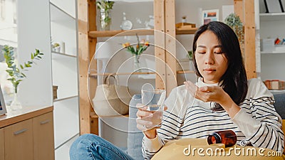 Sick young Asia woman holding pill glass of water take medicine sit on couch at home. Girl taking medicine after doctor order, Stock Photo