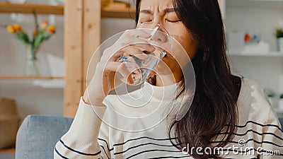 Sick young Asia woman holding pill glass of water take medicine sit on couch at home. Girl taking medicine after doctor order, Stock Photo