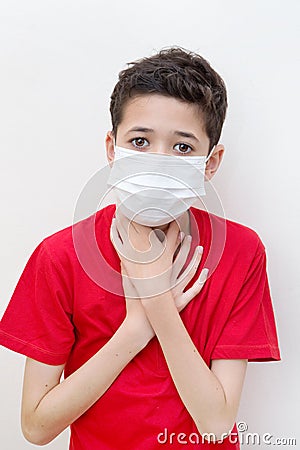 Sick young boy clutches his throat with face mask on. Stock Photo