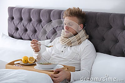 Sick young man eating soup to cure flu in bed Stock Photo