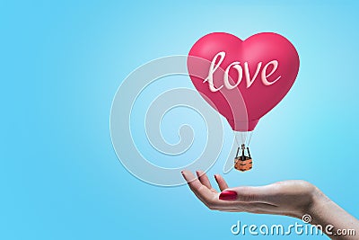 Side close-up of woman`s hand facing up to catch little heart-shaped hot-air balloon with title `love` on it. Stock Photo