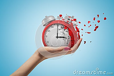 Side closeup of woman`s hand facing up and holding red retro alarm clock that is dissolving into small pieces on light Stock Photo