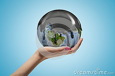 Side closeup of woman`s hand facing up and holding small Earth covered in black oli-like liquid on light blue background Stock Photo