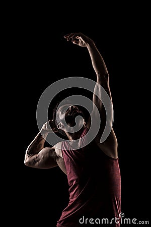 Side lit muscular Caucasian man silhouette. Athlete in red shirt posing against black background Stock Photo