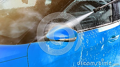 Side mirror of blue car washed in self serve carwash, jet water sprays from high pressure nozzle Stock Photo