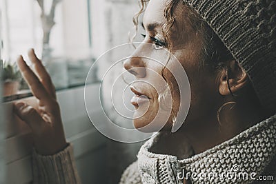 Side portrait close up of young mature woman looking outside the window at home. Concept of waiting and hoping in life. Female Stock Photo