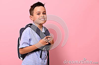 Side portrait of a smiling with toothy smile schoolboy with a school bag on his back on pink background with copy space. Back to Stock Photo