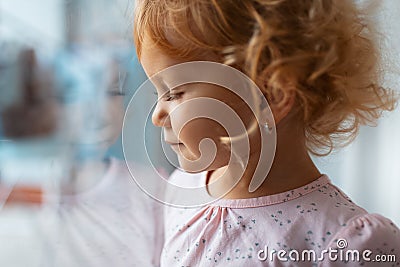 Side portrait of thoughtful child girl near window. Reflection of face on glass. Stock Photo