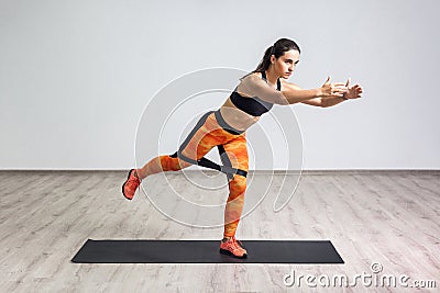 Side portrait view of beautiful young woman wearing black tank top and orange leggings, workout alone against white wall, doing Stock Photo
