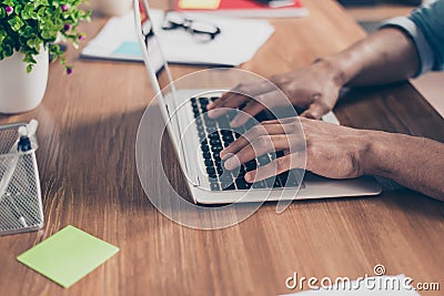 Side profile cropped photo of afro american`s businessman hands on keyboard of laptop on a wooden desk top, busy typing the data Stock Photo