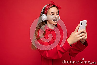 Side-profile photo of smiling Positive attractive brunette girl wearing red hoodie isolated on red background holding Stock Photo