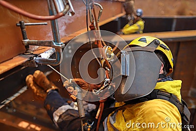 Side shot close up of industrial rope access welder maintenance abseiler wearing fall safety body harness helmet PPE Stock Photo