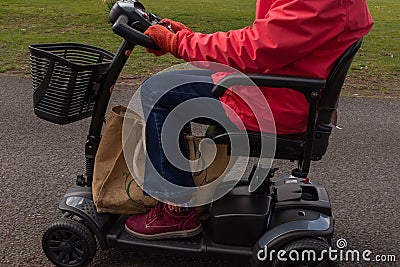 A side on shot of an elderly lady in a red coat enjoying the freedom of an electric mobility scooter Stock Photo