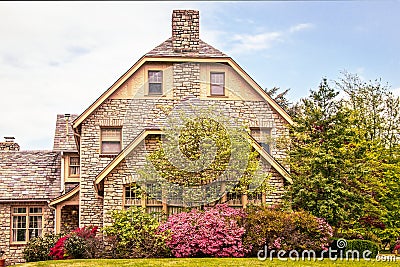 Side of upscale three story rock home with pink azaleas and dogwood tree in full bloom in Springtime Editorial Stock Photo